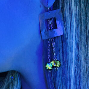 Boucles d’oreilles pendantes dorées à l’or fin avec carré martelé et trois perles lucioles photoluminescentes sur chaîne, collection Cassiopée. Photo prise à la lumière noire.