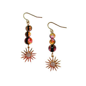 Comme trois petites lucioles guidant la nuit, ces boucles d’oreilles de la collection Perséïdes laissent pendre un trio de perles photoluminescentes dorées et orangées, qui se chargent de lumière avant de la diffuser en douceur. À leur extrémité, une étoile dorée à l’or fin scintille telle une ultime étincelle céleste. Un bijou délicat, rêveur, pensé pour celles qui aiment porter un fragment de ciel.